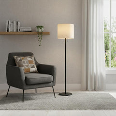60" black and white floor lamp with a white fabric drum shade, positioned next to a gray armchair on a textured rug.