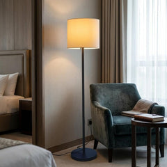 60" black and white floor lamp with a white fabric drum shade, placed next to a green armchair in a cozy room setting.