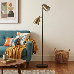 58" black two-light task floor lamp with antiqued brass metal cone shades, set in a cozy living room with a teal couch and de