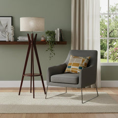 60" brown and white solid wood tripod floor lamp with white fabric drum shade beside a gray armchair and decorative shelf.