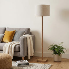 59" Natural Solid Wood Floor Lamp with White Linen Drum Shade beside a cozy sofa, decorated with cushions and a plant.