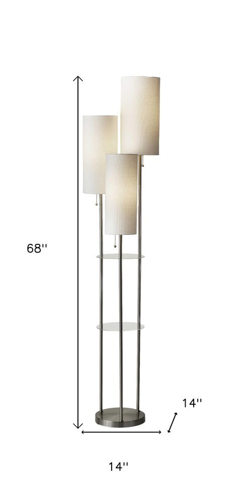 Silver three-light floor lamp with white linen cylinder shades, featuring a sleek design and glass shelves. Height: 68", widt