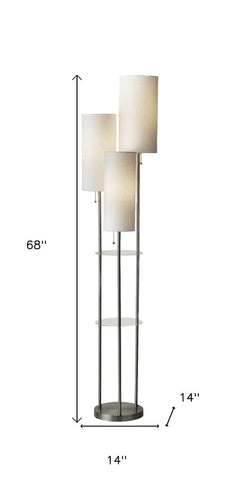 Silver three-light floor lamp with white linen cylinder shades, featuring a sleek design and glass shelves. Height: 68", widt