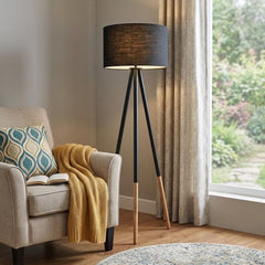 Black Metal Tripod Floor Lamp with Black Fabric Drum Shade, featuring a modern design and wooden accents, beside a cozy armch