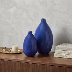 Set of two cobalt ceramic round table vases in varying sizes, displayed on a wooden surface with books and a candle.