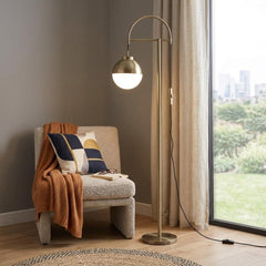 69" Bronze Steel Floor Lamp with a globe shade, featuring a modern design beside a cozy chair and decorative throw.