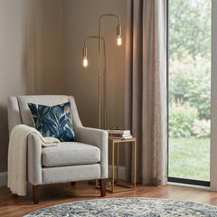 63" Two Light Torchiere Floor Lamp with a sleek gold finish beside a cozy armchair and side table with books.