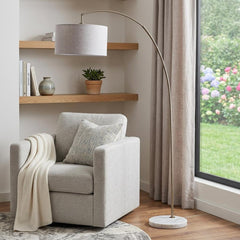 86" beige and antique gold arched floor lamp with gray drum shade, positioned next to a cozy chair and a window.
