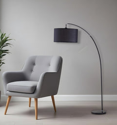86" Black Metal Arc Floor Lamp with a black fabric drum shade, positioned next to a modern gray armchair in a stylish interio