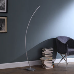 62" Silver and Soft White Arc LED Floor Lamp with a sleek design, positioned beside a stack of books and a chair.