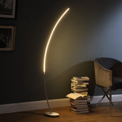 62" Silver and Soft White Arc LED Floor Lamp with a sleek design, illuminating a cozy reading corner beside a stack of books.