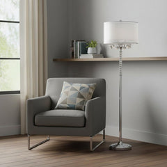 63" Silver Three Light Candelabra Floor Lamp with White Fabric Drum Shade beside a modern gray armchair in a bright room.