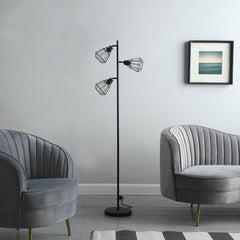 66" Black Metal Three Light Tree Floor Lamp with black metal cage shades, positioned between two stylish gray armchairs.