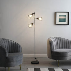 66" Black Metal Three Light Tree Floor Lamp with black metal cage shades, positioned between two gray upholstered chairs in a
