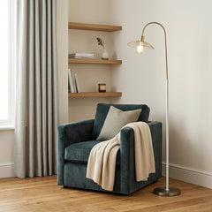 64" Gold and White Arched Floor Lamp with a gold metal cage shade beside a cozy armchair draped with a blanket.