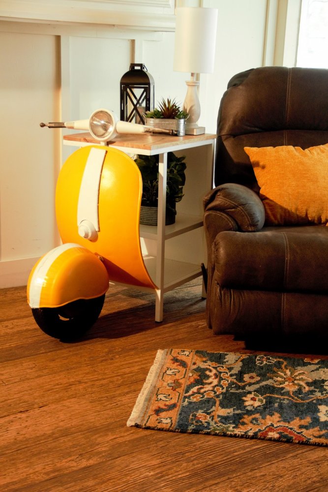Yellow Wood And Metal Mini Scooter End or Side Table featuring a playful scooter design, placed beside a cozy armchair.