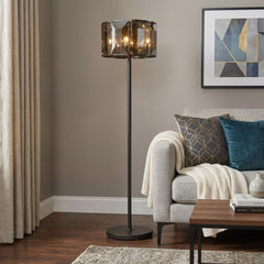 68" Dark Bronze Floor Lamp with amber beveled glass drum shade, standing beside a cozy sofa with decorative pillows and a cof