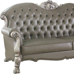96" Bone Faux Leather Sofa with tufted back, ornate silver accents, and white legs, includes toss pillows for added comfort.