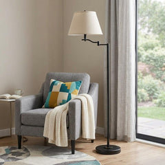 60" Bronze Swing Arm Floor Lamp with Beige Fabric Empire Shade beside a gray armchair, featuring a colorful pillow and a cozy