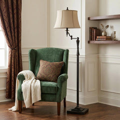 61" Bronze Swing Arm Floor Lamp with a brown square shade, positioned next to a green armchair and decorative elements in a c