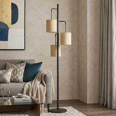 72" Bronze Three Light Traditional Floor Lamp with Beige Drum Shades, set in a cozy living room with a sofa and decor.