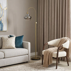 61" Brass Adjustable Arc Floor Lamp with antiqued brass mirrored glass shade, set beside a cozy chair and sofa in a stylish l