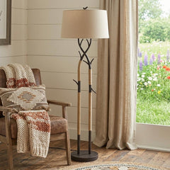 55" black metal and rope tree branch floor lamp with tan fabric shade, set beside a cozy chair in a bright, floral room.