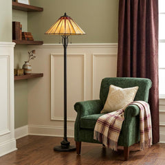 61" bronze floor lamp with red and ivory abstract Tiffany glass shade beside a green armchair with a plaid throw.
