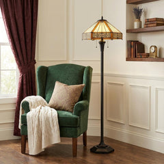 60" bronze floor lamp with orange and ivory abstract Tiffany glass shade beside a green armchair in a cozy room setting.