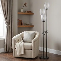 71" black three-light traditional floor lamp with clear glass shades, beside a cozy armchair and decorative shelves.