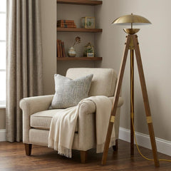55" Brass Tripod Floor Lamp with Antiqued Brass Dome Shade beside a cozy armchair and decorative shelves in a warm room setti
