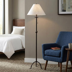 57" black traditional floor lamp with a white empire shade, placed beside a blue armchair in a cozy bedroom setting.