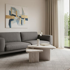 Set of two natural solid wood triangle pedestal nested coffee tables in a modern living room with a gray sofa and abstract ar