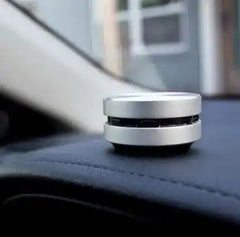 Silver Humbird Bone Conducting Speaker placed on car dashboard, demonstrating its portability and surface-based sound output.